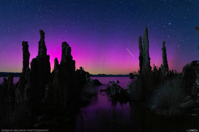Mono Lake tufa landscape with a magenta, yellow, and blue aurora reflected on the lake's water. The ISS (I think) is streaking through.
