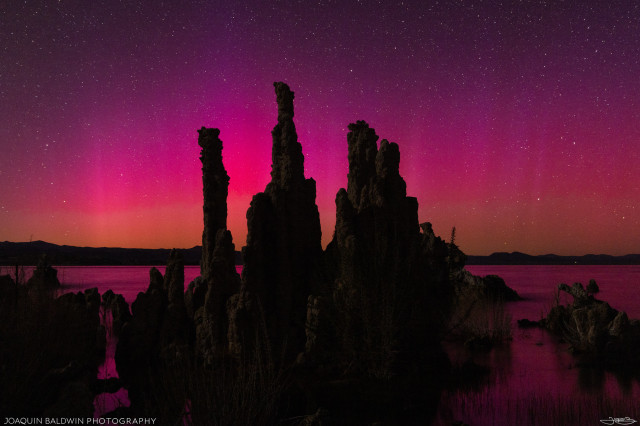 A cluster of Mono Lake tufa silhouetted over a bright pink and red aurora. The light pillars are not too defined, but the colors are intense and reflect on the lake.
