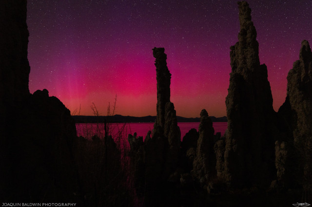 More Mono Lake tufa towers with a pink, yellow, and red aurora glowing softly behind them.
