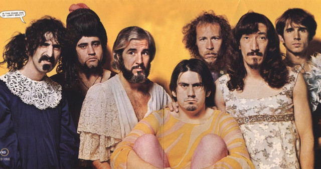 A picture of Frank Zappa and the Mothers of Invention. They are scraggly men with long hair. Most are wearing dresses