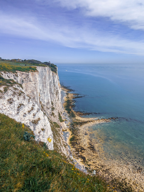 The white cliffs of Dover with a backdrop of a partly cloudy sky and the ocean turquoise, fading into the horizon.