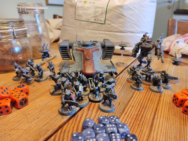 Some Tau plastic models on a wooden table. The models are mostly painted grey, with red details. 