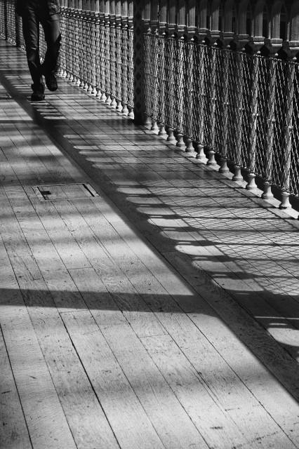 Sunlight casts a fascinating shadow of the ornate metal railings inside the National Museum in Edinburgh. The lower half of a person approaches from the top left corner.