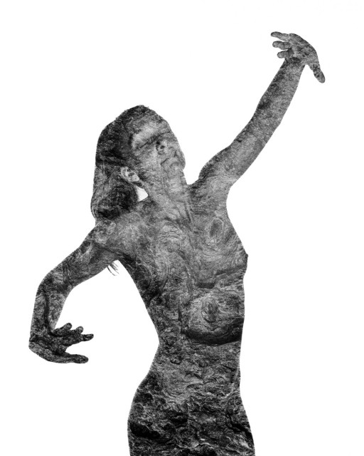 A naked woman is standing in front of a white background, her arms outstretched. Her skin is blended with rock textures. Black and white. 