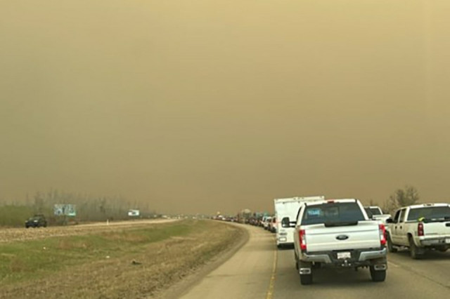 a line of vehicles disappears into the distance under grey/brown skies of smoke