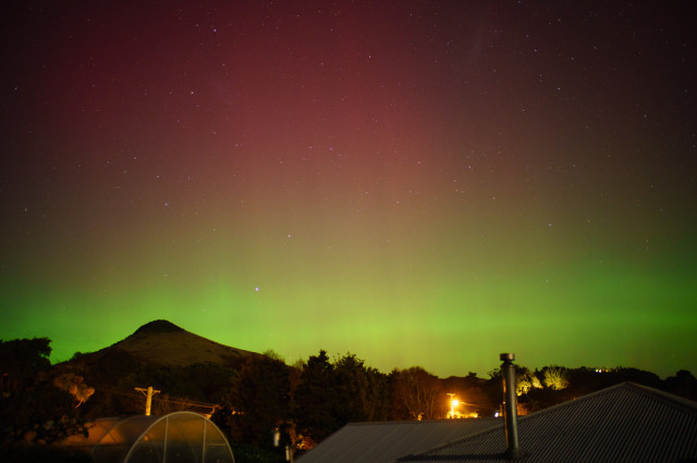 Green aurora dominates the sky against a foreground of suburban hills in Dunedin 