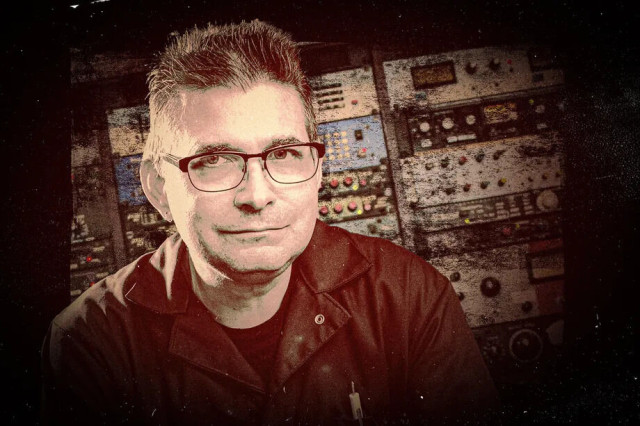A processed photo of Steve Albini slightly smiling in front of a bank of electronic music production gear.