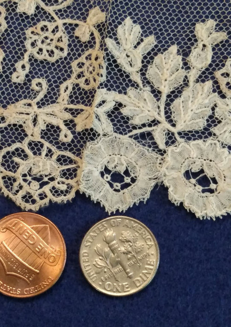 A close up of the now-unstuck lace on a blue felt backing for contrast. It shows the floral edge of the lace and includes two American coins for scale. The flowers are about the size of a 10 cent silver piece. 

The threads are incredibly thin, and the flower is worked with a heavier outline edge. There are also tiny picot decorations on the outside edge. 

There are coin-sized flowers on the edge and smaller ones as you go up, as well as some leaves and vine details. Some of this seems to be embroidered on the netting and some additional needle lace details. 