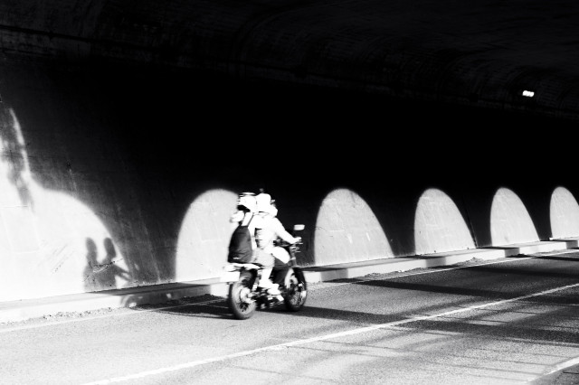 Two people on a motorbike going through a tunnel.