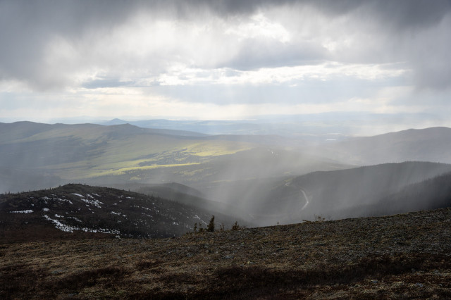 Scenic view from Wickersham Dome showing the Elliot Highway winding through the valley, with a mix of forested and snow-patched terrain under a cloudy sky
