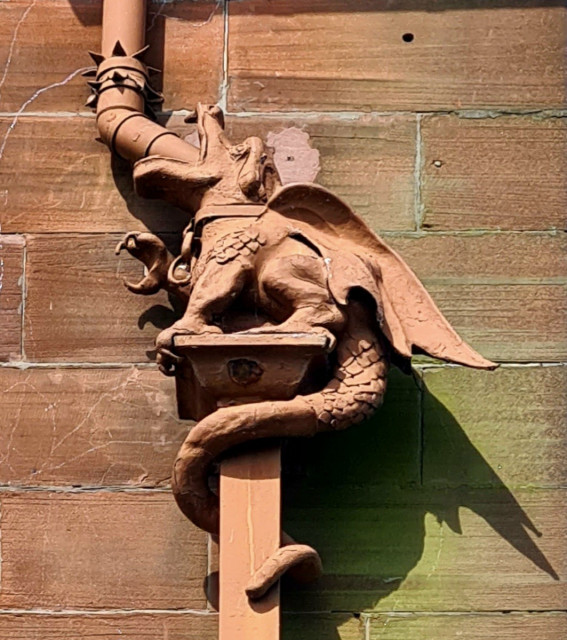 A drainpipe with a cast iron dragon set into an angle on it, so that the water enters through its mouth and out the pipe the dragonnis standing on.