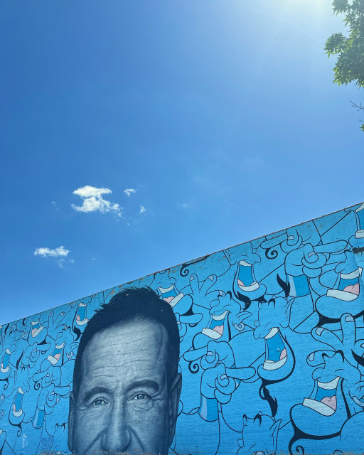 Close crop of a mural featuring Robin Williams. The background features various iterations of the genie character he voiced from Disney’s Aladdin. 