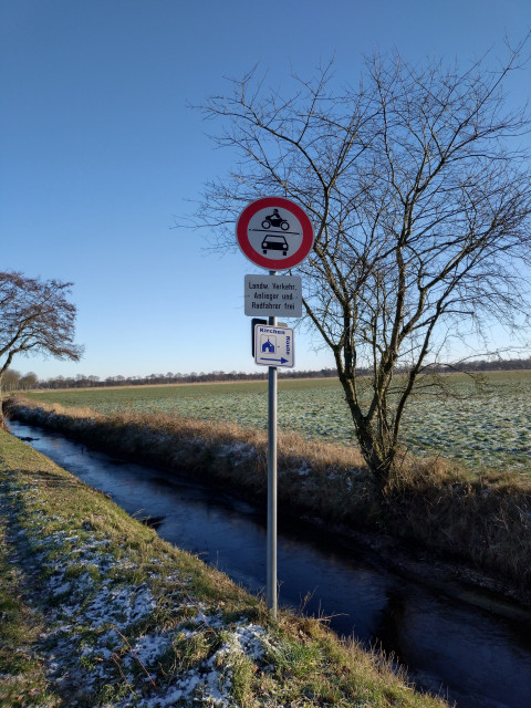 Foto von winterlichen Feldern, einem Graben und davor ein Verkehrsschild Verbotsschild für Motorräder und Auto, darunter der Zusatz landwirtschaftlicher Verkehr - Anlieger und Radfahrer frei.