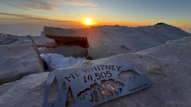A summit plaque for Mount Whitney laying on a rock on the summit during sunrise