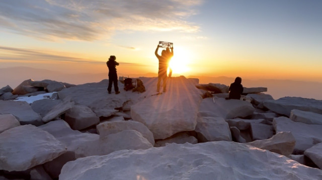 Hikers hold up the summit plaque for a photo with sunrise on the summit of Mount Whitney 