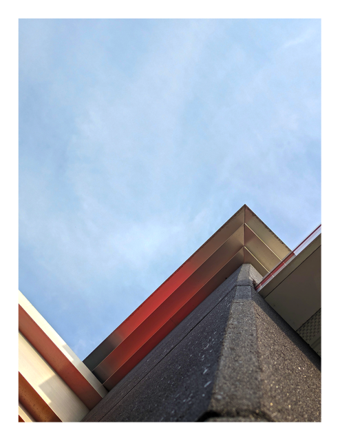 abstract. low-angle view up a cement support column for a building, to the roof corner and decorative elements. unformed clouds cover the blue sky in the background.