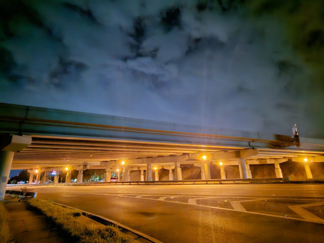 Late night looking upon an interstate highway overpass bridge illuminated with yellowish lighting, highlighting the massive stone structure beneath a spooky, cloudy, night sky.