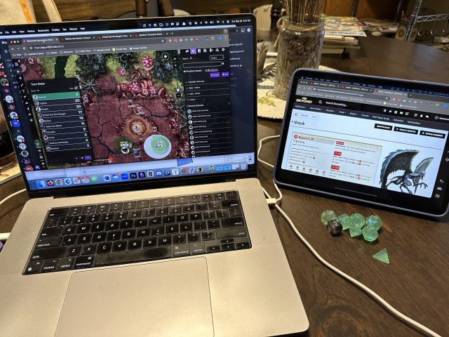 A MacBook Pro on the left with a Roll20 on screen, and an iPad, acting as a second screen, on the right with a monster reference.