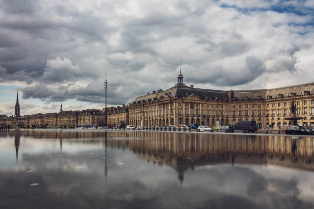 Fotografía a color donde se ve parte de la Place de la Bourse (Burdeos) con reflejos y nubes.