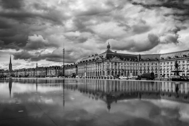 Fotografía en B&N donde se ve parte de la Place de la Bourse (Burdeos) con reflejos y nubes.
