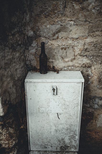 Alter Schaltschrank mit einer Bierflasche oben drauf, dahinter eine Steinwand.