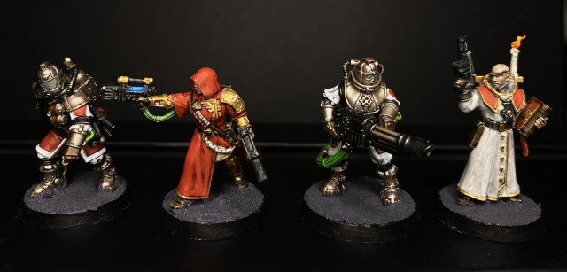 Four intricately painted miniature figures from a tabletop game, each in distinctive armor and poses, standing on black bases.