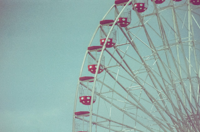 Part of an empty ferris wheel. Red polka dot buckets against a cyan sky.
