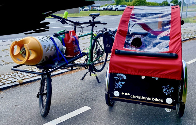 Two cargobikes. One with a propane tank and some synthetic fuel. The other with a tiny human and some groceries.