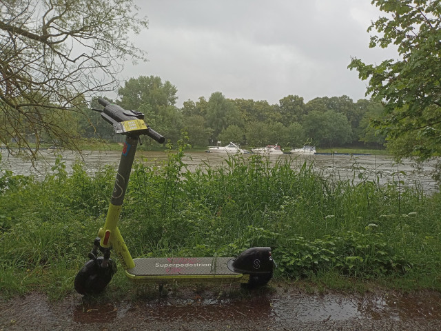 Möglicherweise einer der erste Sachschäden im Hochwasser: Elektromietroller im Regen auf dem Uferweg der Holzlände. Im Hintergrund Motorboote am anderen Donauufer.