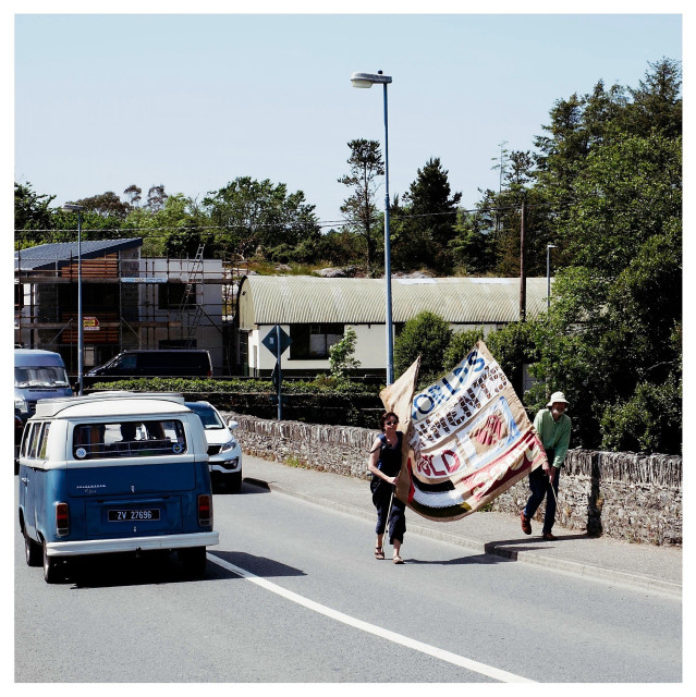 Two people walking up onto the Ballydehob bridge with their banner of solidarity with the people of Palestine as a classic blue and white VW Camper heads in the opposite direction.