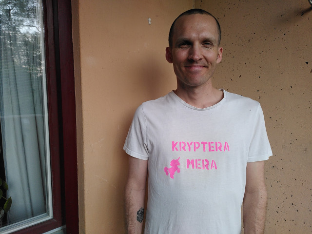 Jag i en vit t-shirt med rosa tryck. Det står KRYPTERA MERA och en bild på en enhörning