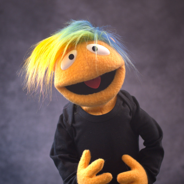 A human like nonbinary puppet character with rainbow hair