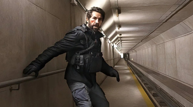 Scott Adkins in a long tunnel. He looks apprehensive and has a boo boo on his cheek.