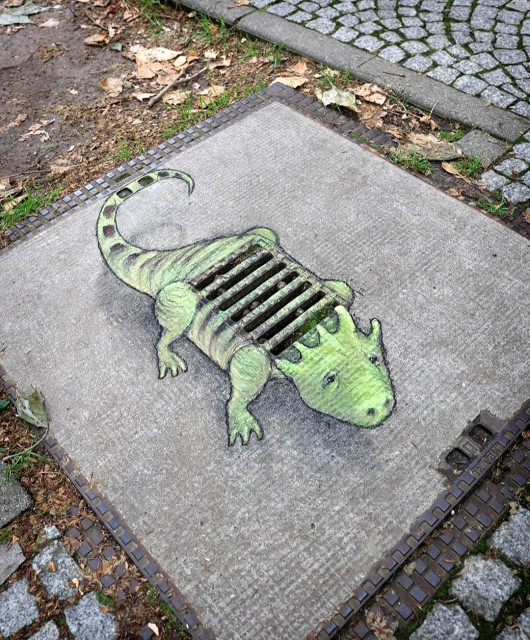 Streetart. A green dinosaur has been drawn in chalk on the sidewalk over a cover with a grid. It looks a bit like a prehistoric crocodile with four small humps on its head and a long tail. The real grid serves as the dinosaur's armored body. But it looks very friendly and is called Rosie. Title: "Rosie doesn't speak very much, but she has a lot of courage and shows grate backbone."