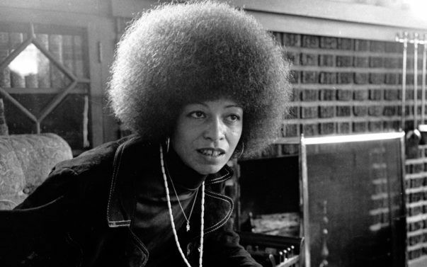 Angela Davis in the early 1970s. She is a black woman with a large 'fro, wearing denims.