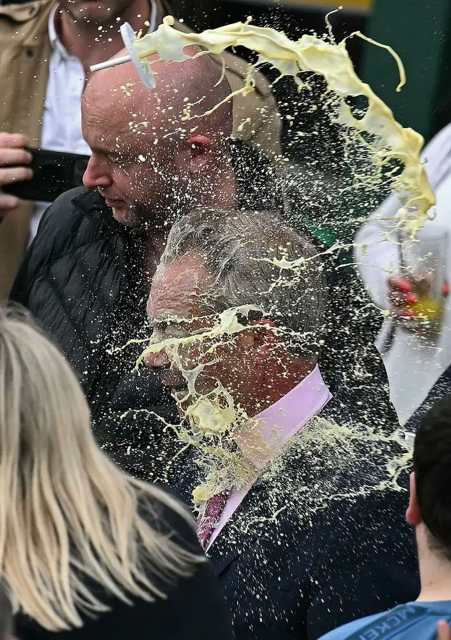 A beautiful piece of art. The lid and straw of a milkshake arcs through the air. The milkshake trails behind and disperses onto the man with Russian talking points, global warming denial, and Brexiteer known as Nigel Farage.