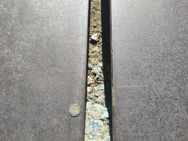 Ein 2-Euro-Stück liegt zur Darstellung der Verhältnisse neben dem Spalt. Er ist etwa dreimal so breit wie die Münze.