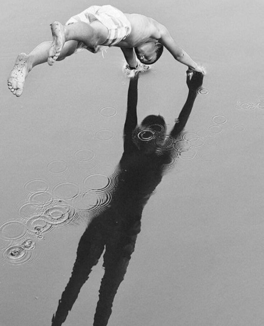 Photograph. A black and white photo of a boy jumping into the water where the shadow of a woman can be seen. Perfect timing makes the photo "special". The shadow of a woman with raised arms, standing on land, can be seen on the surface of the water. A boy in swimming trunks jumps into the water and hits the water with his raised arms exactly where the shadow's hands are. A few circles form on the surface of the water.
Info: Kertesz, Andre (1894-1985) 
was a Hungarian-born photographer known for his groundbreaking contributions to photographic composition and the photo essay. In the early years of his career, his then-unorthodox camera angles and style prevented his work from gaining wider recognition