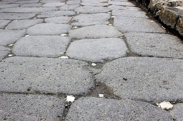 This is a photo of a road in the ruins in Pompeii.

It shows a close-up of large dark grey paving stones, all of roughly the same size but without proper shaping.

Between the large pavers are small, white stones, roughly the size of 2€ or 1 US$ coin.
They are set inside the crevasses left between the large stones.