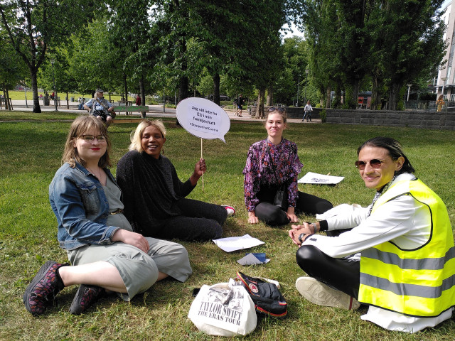 Fyra personer sitter på gräset i en park och håller upp en pratbubbla mef texten "Jag vill inte ha EU i min familjechatt #StoppaChatControl"