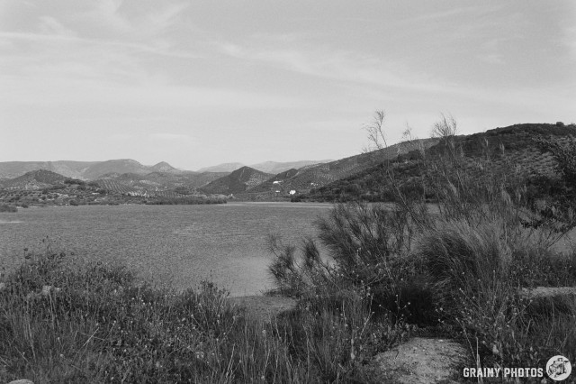 A black-and-white film photo across a lake with mountains in the distance.