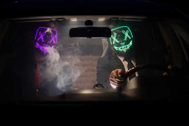 Picture of two men sitting in a car with masks on. 