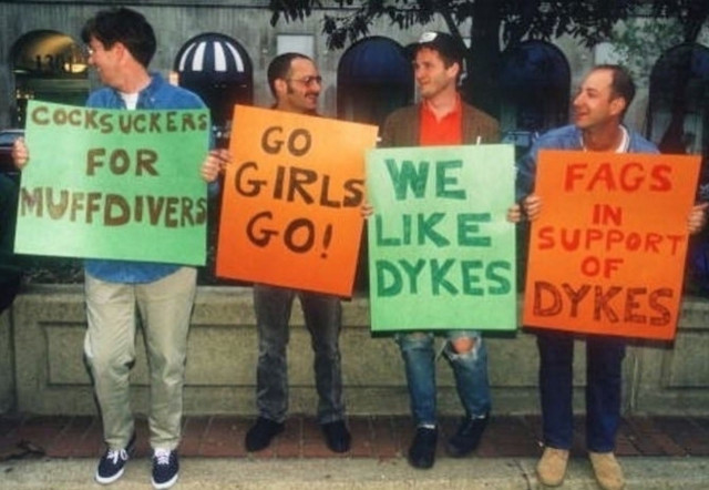 Gay male supporters at the first Dyke March in Washington DC in 1993. One is holding a sign "cocksuckers for muffdivers" another "Go Girls Go" another "we like dykes" and another "fags in support of dykes"