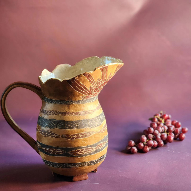 Handmade, rustically decorated pitcher with a rich purple background and grapes.