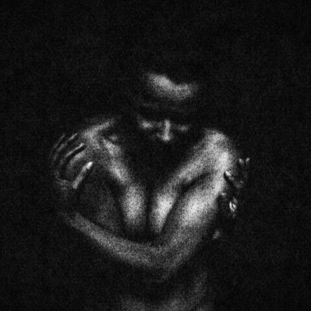 A naked woman has her arms wrapped around her torso. The texture of the film creates criss-crosses over her skin. Black and white. 