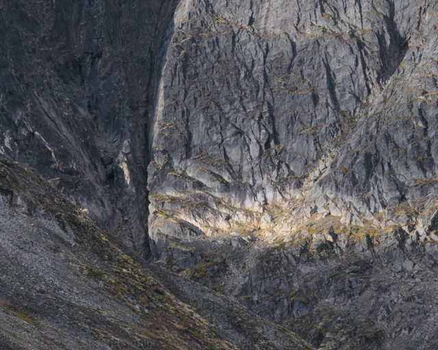 An intimate shot of the cirque of a massive rock cliff with dappled light.