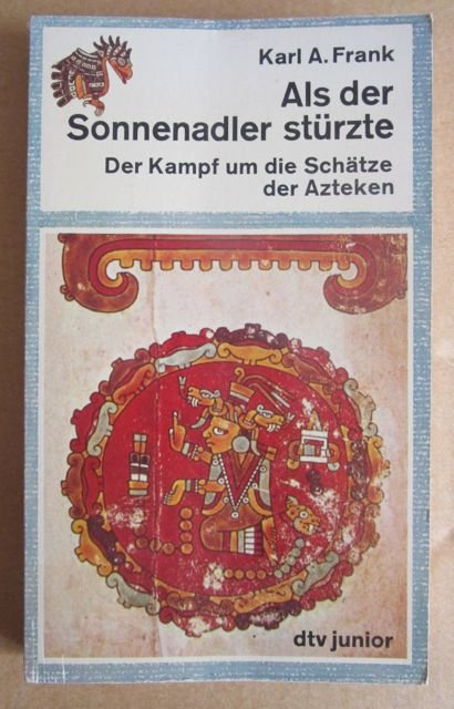 A paper back book 

Above author and title

Below precolombian art:

A red ornamented Sun disk. Inside a richly dressed person kneeling making hand gestures