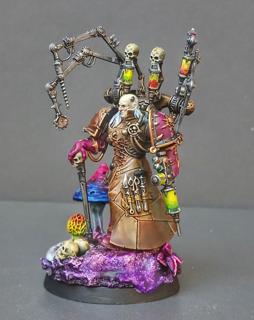 Painted miniature of Fabius Bile. He is walking over a rocky base (mostly painted in purple tones, but some are green/brown, too) with giant mushrooms and skulls. He is holding Torment and some kind of Injector. Front View. 
