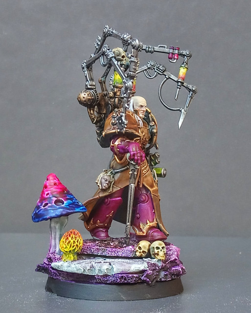 Painted miniature of Fabius Bile. He is walking over a rocky base (mostly painted in purple tones, but some are green/brown, too) with giant mushrooms and skulls. He is holding Torment and some kind of Injector. Side View. 