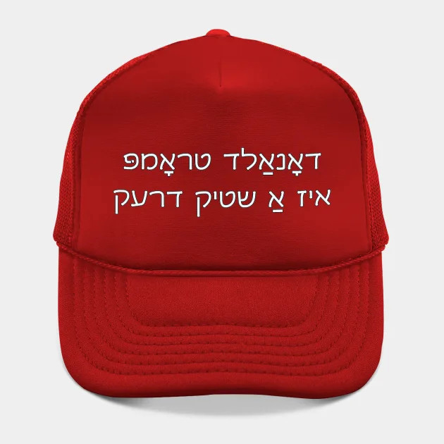 A red hat reading "Donald Trump is a piece of shit" in white Yiddish text